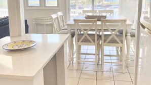Eine helle Küche mit einer großen Kochinsel, weißen Schränken und Blick aufs Meer.