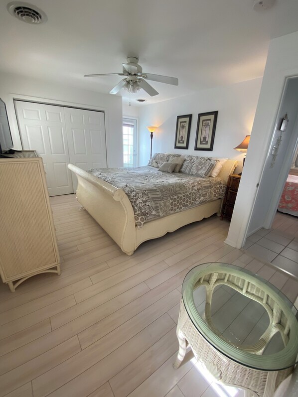 A bedroom with a bed, a ceiling fan, a dresser, and a glass table.