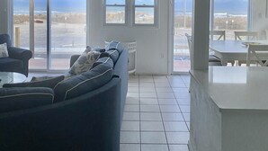 Ein geräumiges Wohnzimmer mit einer großen Couch, einem Essbereich und Blick auf den Strand durch große Fenster.