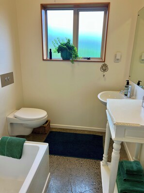 A bathroom with a toilet, sink, and bathtub, a window with a view, and a potted plant on the windowsill. - Pet, Child and ECO Friendly Holiday Home (Mapua (Ruby Bay))