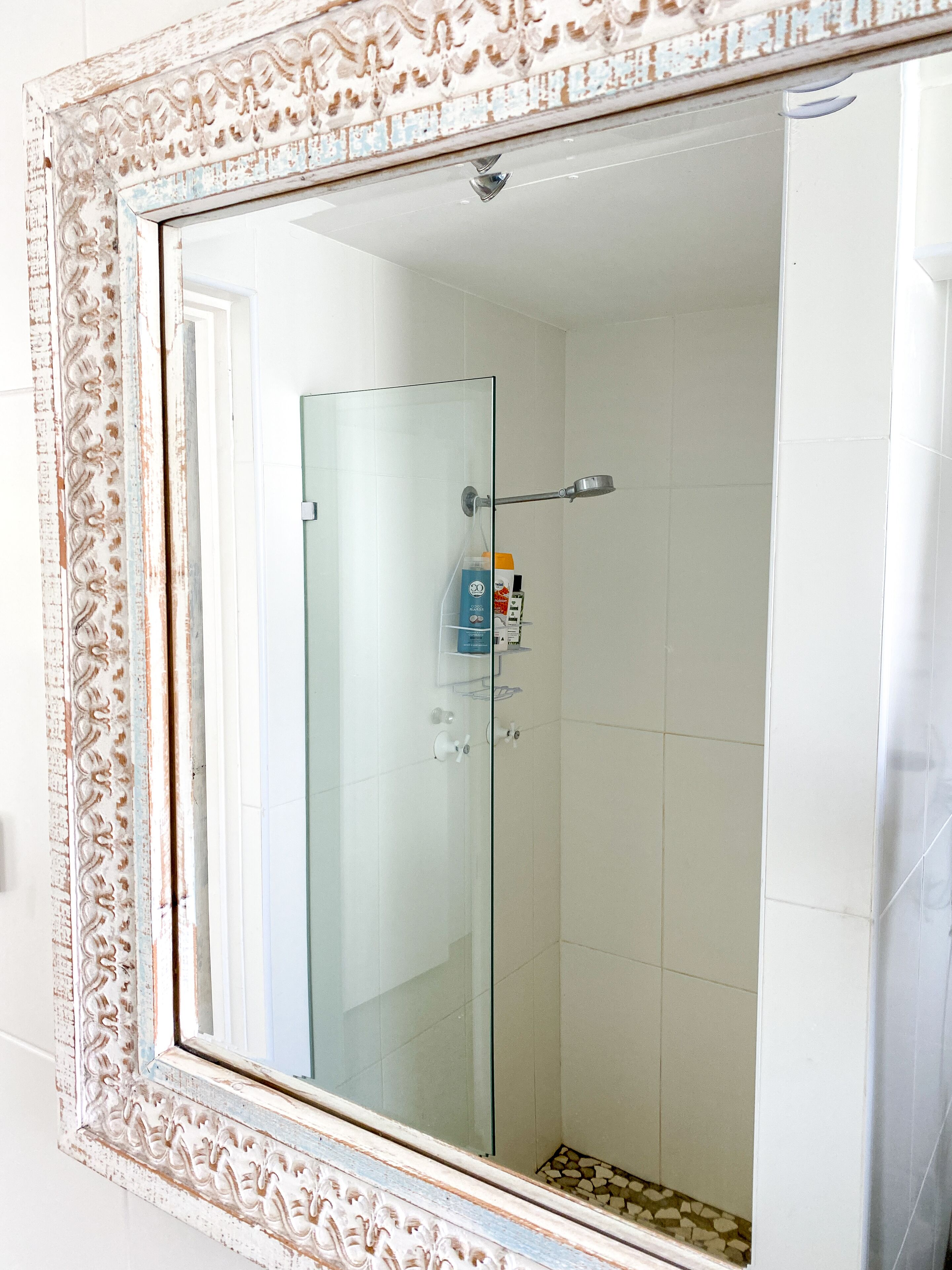 Un bagno con box doccia in vetro, pareti rivestite di piastrelle bianche e una cornice decorativa attorno allo specchio.