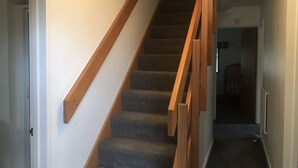 Eine Treppe mit hölzernen Geländern und Teppichstufen, die zu einer Zwischenebene führt.