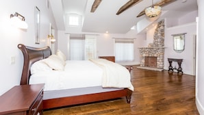 Un dormitorio con una cama grande, vigas de madera, chimenea de piedra y un candelabro colgante.