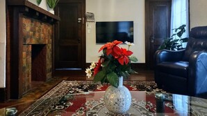 Un salon avec une cheminée, un téléviseur, un fauteuil en cuir noir et un vase rempli de fleurs.