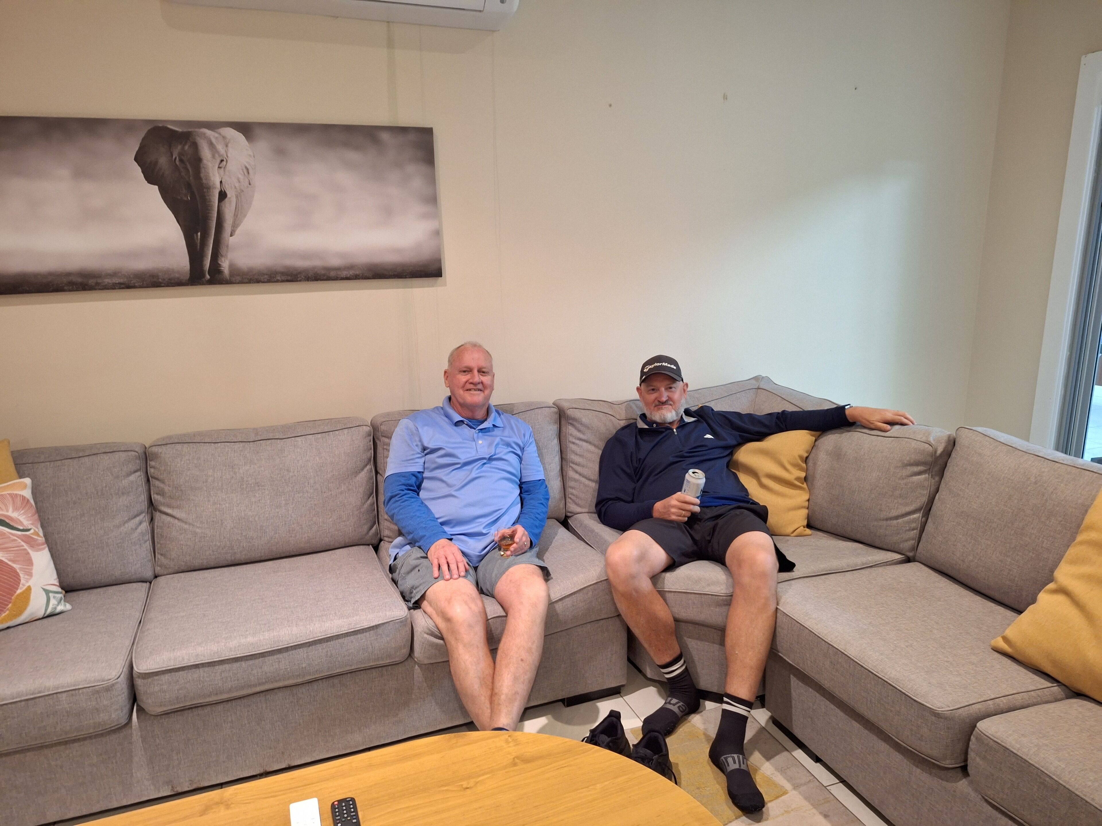 Two people sitting on a grey sofa in a living room with a large abstract painting on the wall.