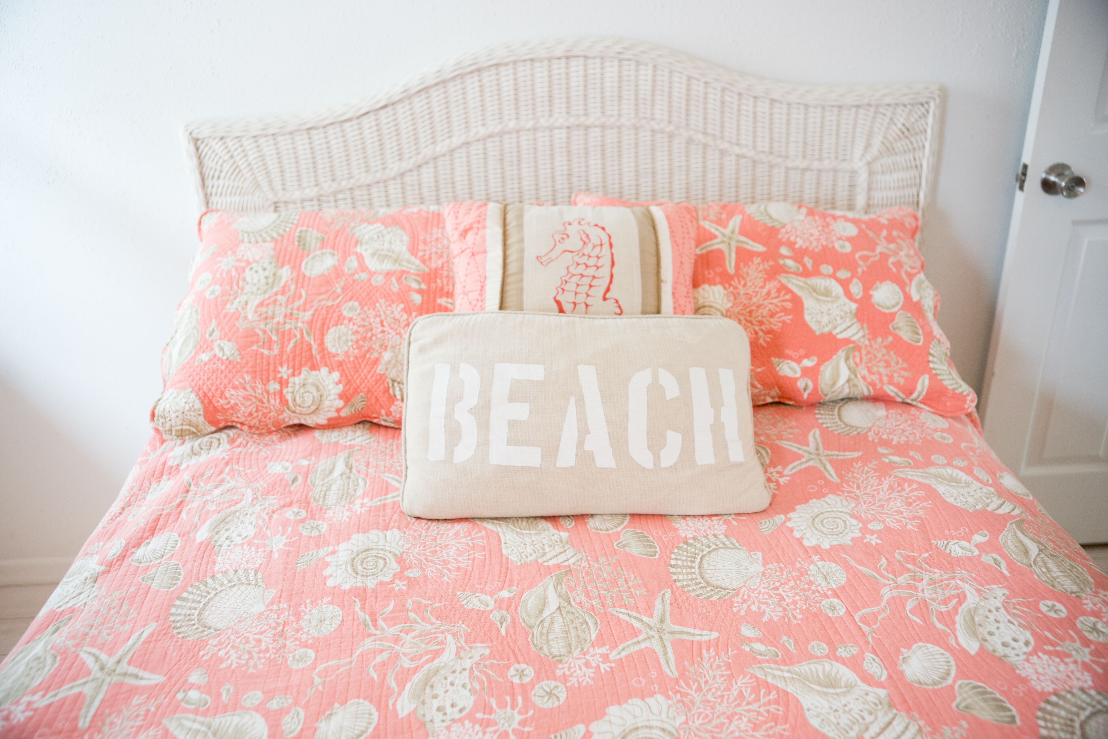 A bed with a floral patterned bedspread, a pillow with the word 'BEACH' on it, and a headboard.