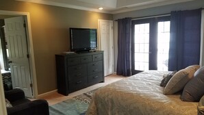 Un dormitorio con cama, cómoda, televisor y ventana con cortinas.