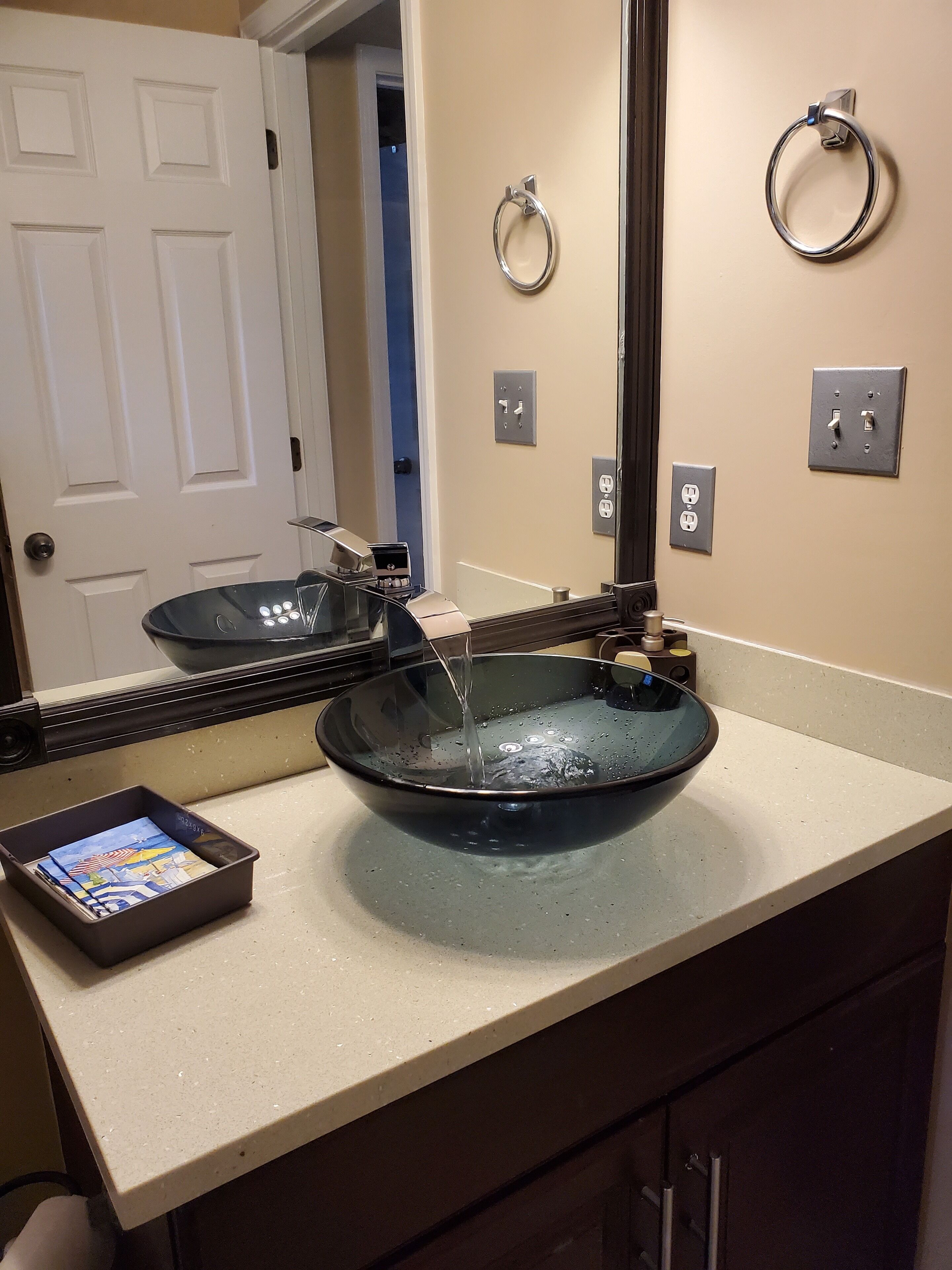 A bathroom with a large, round, dark blue sink, a mirror, and a small tray with cards.