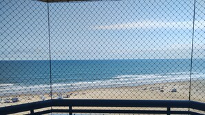 A beach view from a balcony with a tiled floor and a chain-link fence.