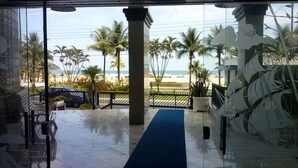 A view from inside a building to a beach with palm trees and a clear sky.