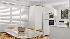 Moderni keittiö, jossa on valkoiset kaapit, sisäänrakennettu uuni sekä ruokailutila, jossa on marmoripöytä ja puutuolit.