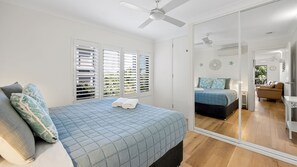 Ein Schlafzimmer mit einem Bett, einem Deckenventilator und einem großen Spiegel, der den Raum reflektiert.