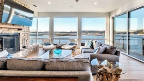 Un salón espacioso con chimenea de piedra, asientos cómodos, un televisor grande y vistas al agua.