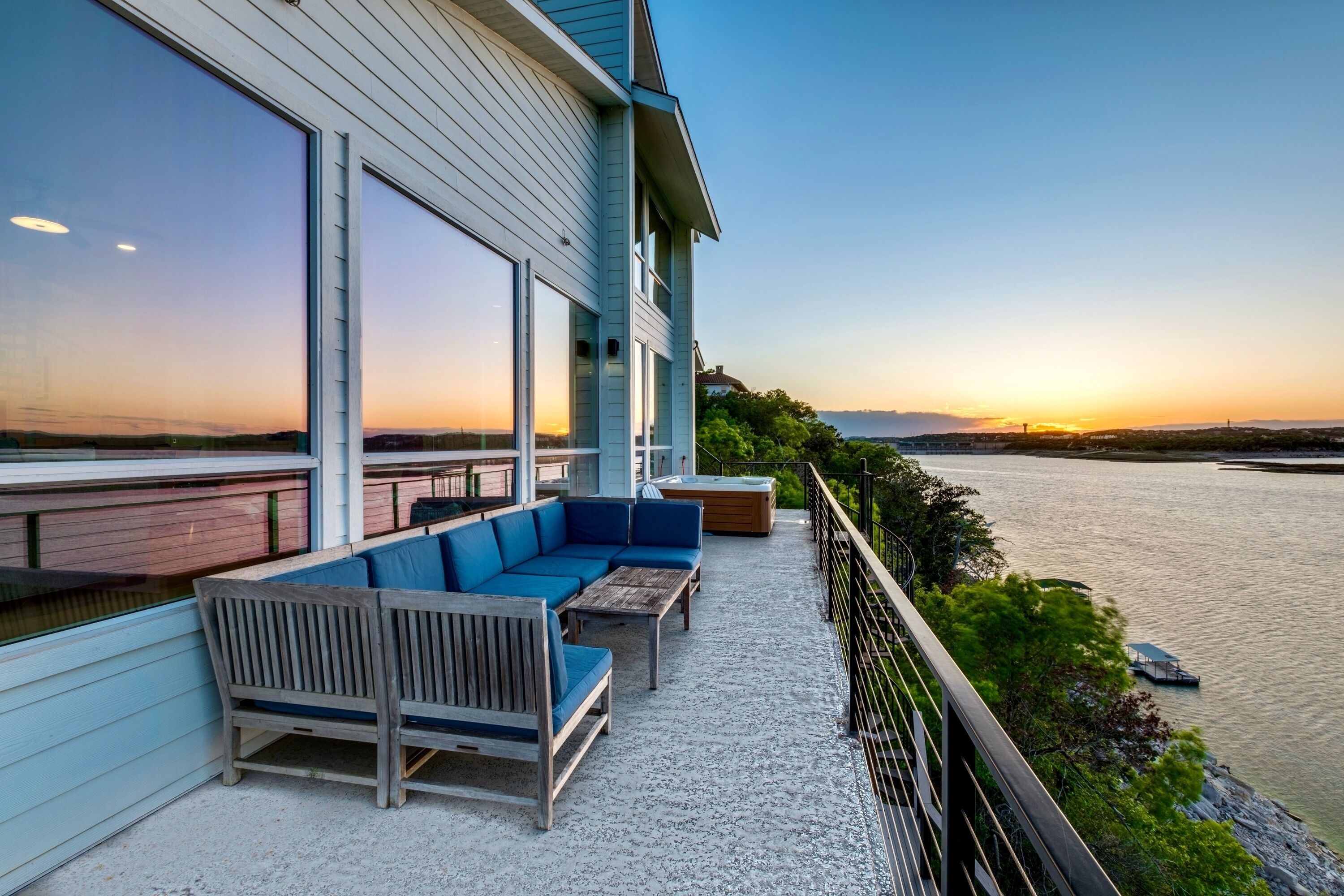 A balcony with a blue sofa and a wooden table, overlooking a body of water and a distant shoreline.