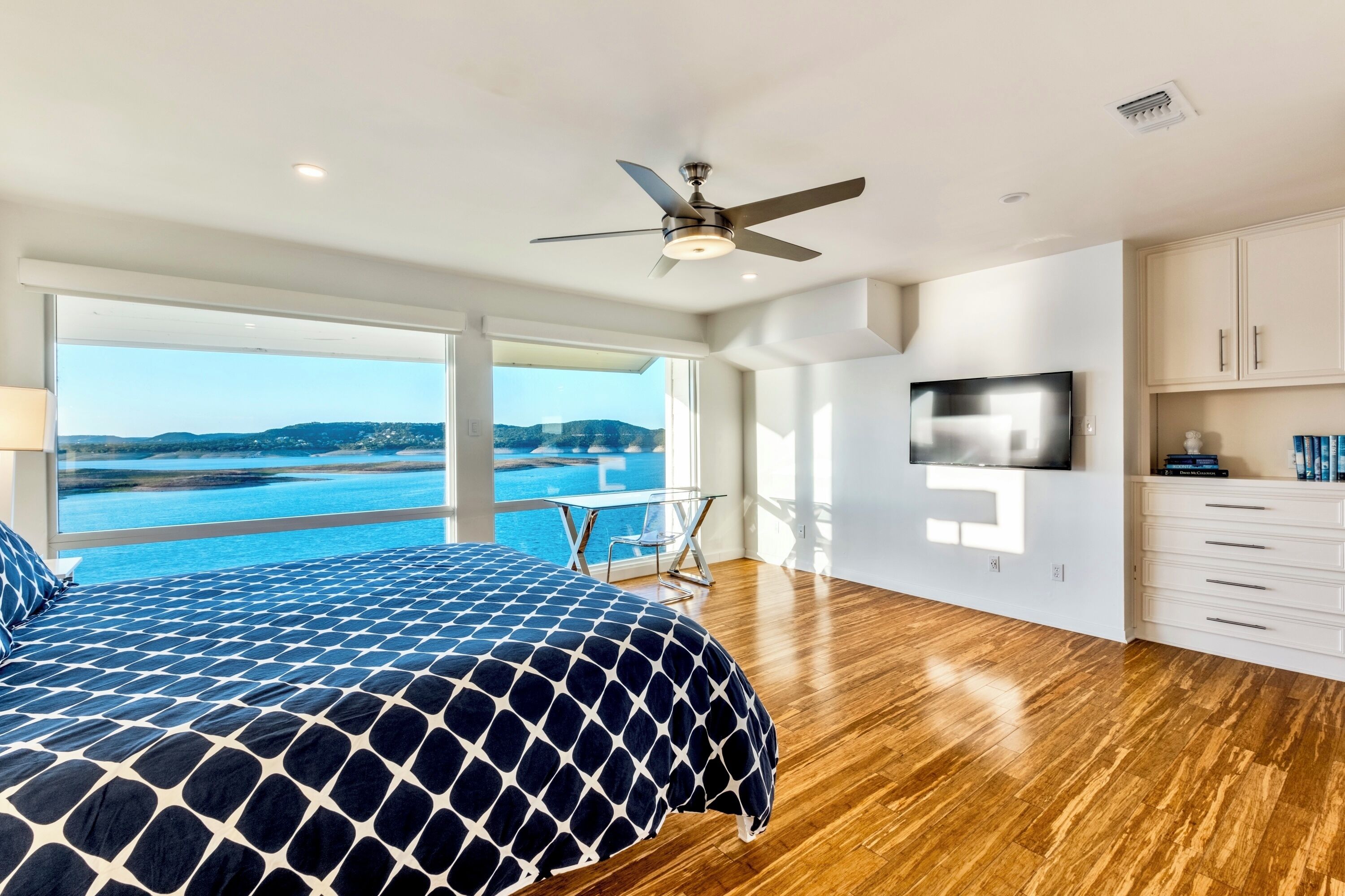 A bedroom with a large bed, a ceiling fan, a TV, and a view of the sea.