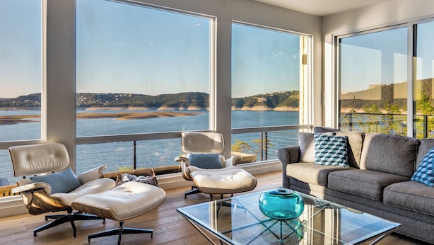 Una sala de estar moderna con ventanas amplias, un sofá de cuero, una mesa de centro de vidrio y vistas a una masa de agua.