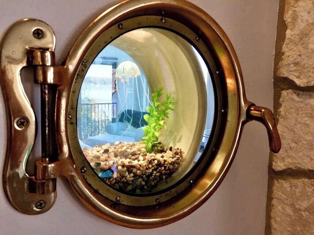 A round, brass-framed window with a view of a balcony and a plant.