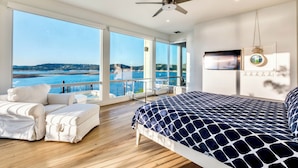 Un dormitorio con una cama grande, ventilador de techo y televisor. Tiene un balcón con vista al mar.