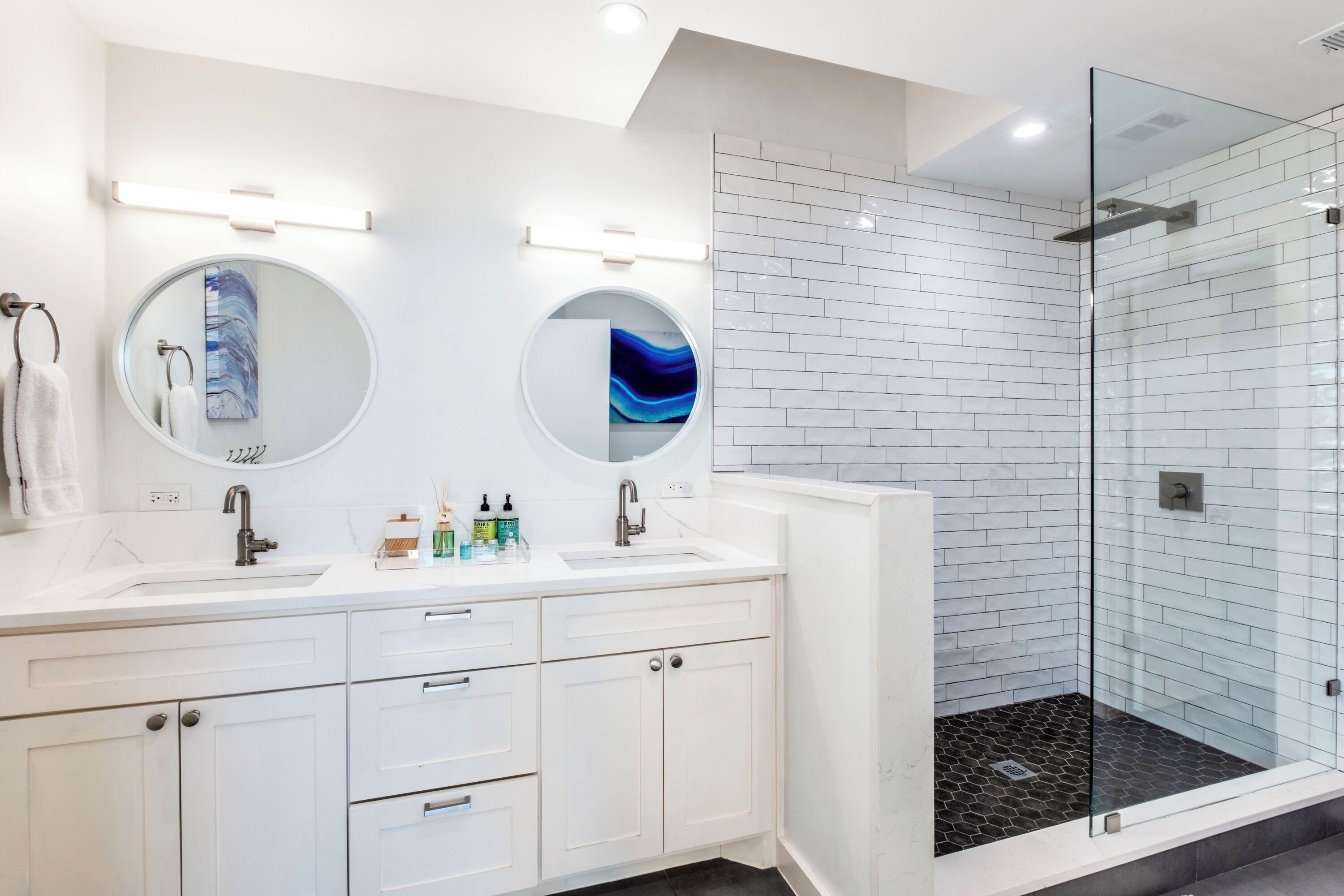 A modern bathroom with two sinks, a glass shower enclosure, and a white tiled backsplash.