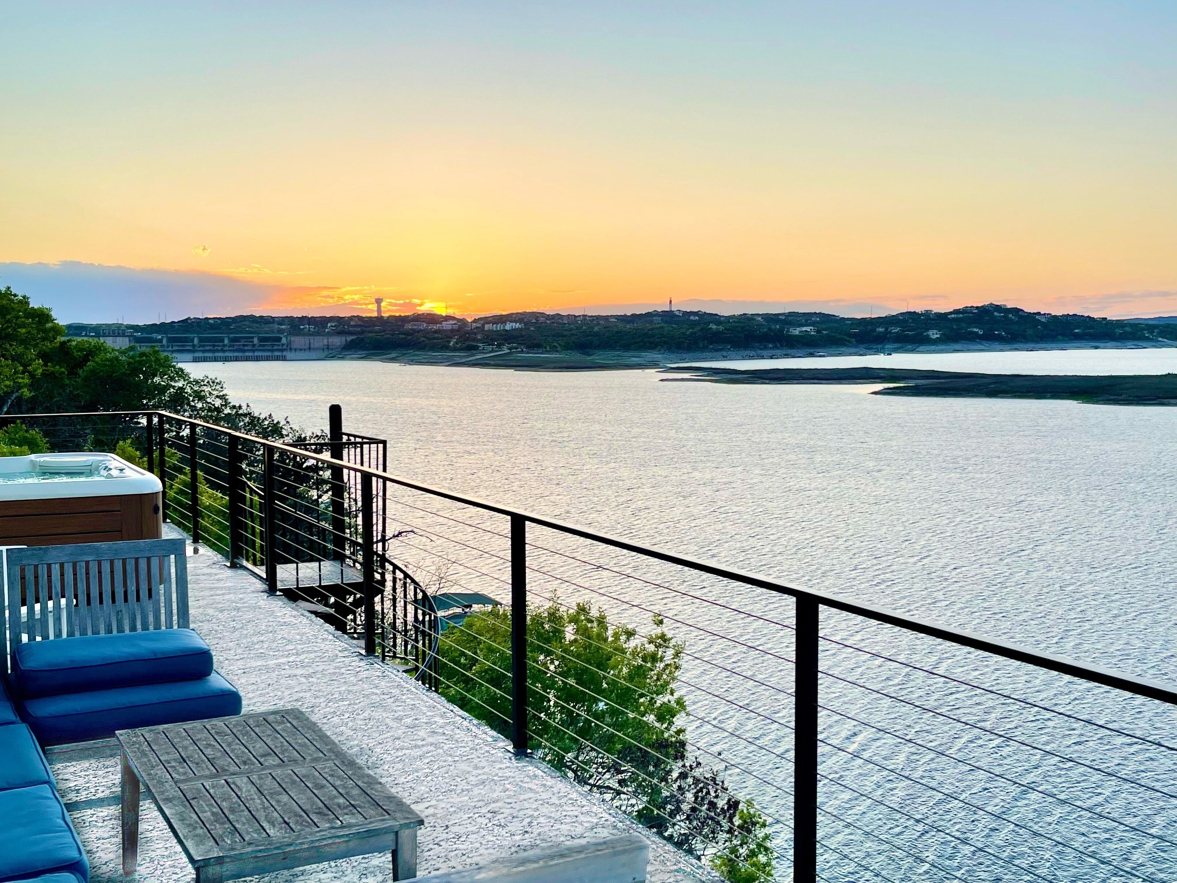Terraza frente al agua con jacuzzi, zona de estar y vistas al atardecer sobre el agua.