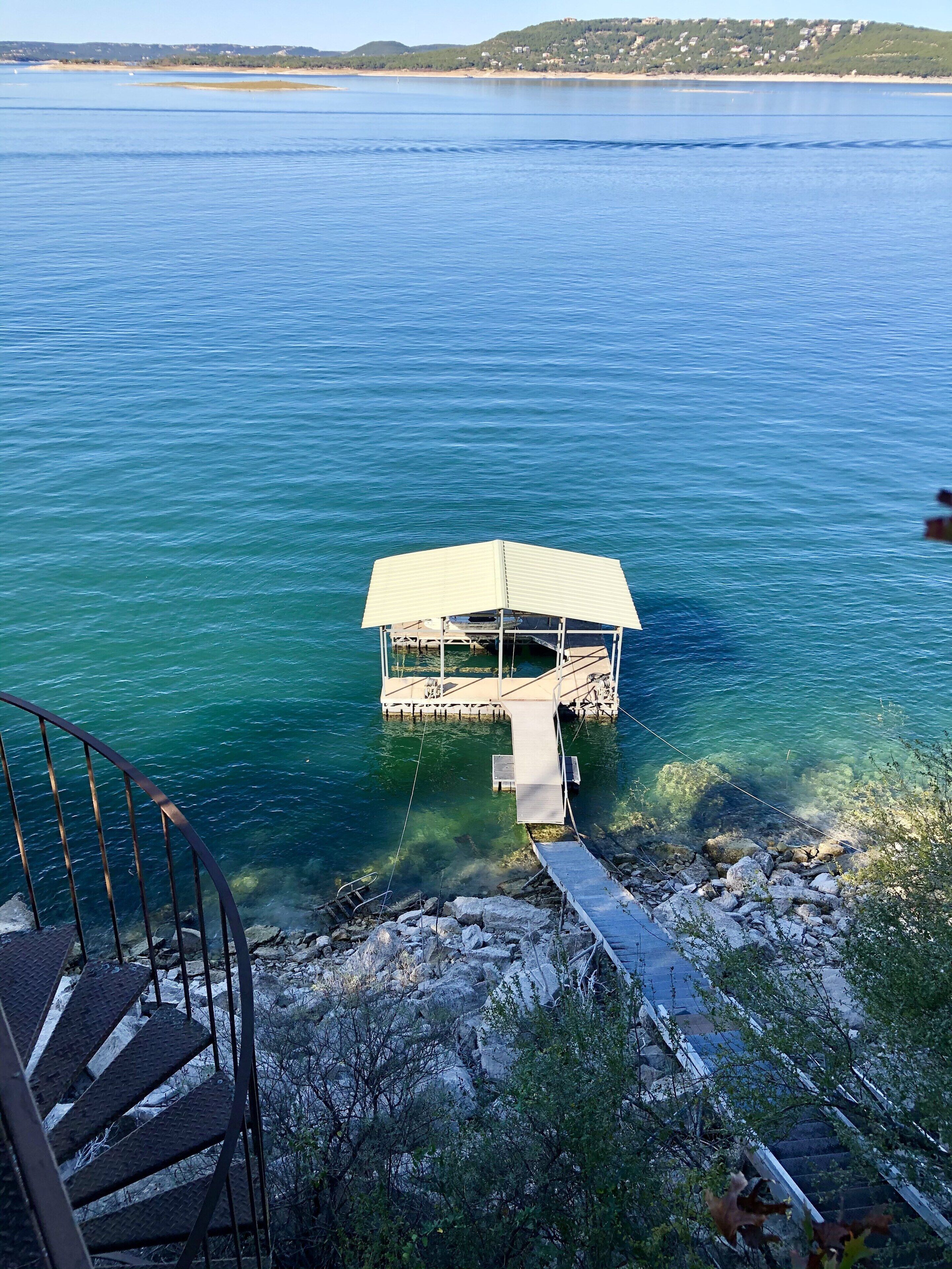 Une propriété située au bord de l’eau, avec une jetée s’avançant dans un lac aux eaux d’un bleu limpide, le tout entouré d’un paysage rocheux et d’une végétation luxuriante.