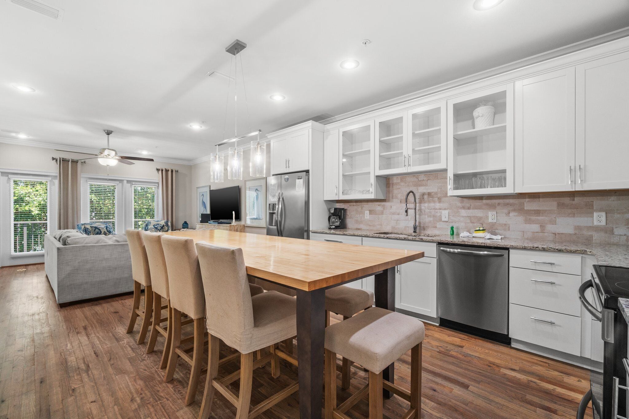 A modern kitchen with white cabinets, a wooden dining table, and a built-in oven.