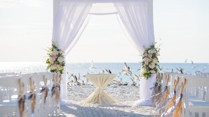 Decoración de boda en la playa, con un arco blanco, arreglos florales y una mesa.