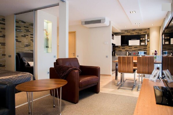 Een moderne woonkamer met een bruine leren bank, een houten salontafel en een eethoek met houten stoelen en een houten tafel.