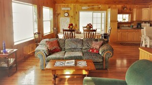 A cabin interior with a wooden ceiling, a dining area with a table and chairs, a kitchen with cabinets and appliances, and a living room with a sofa and coffee table. - BLOW OUT-SALE PRICES!  3 DAY FOLIAGE,Fishing, Dock, Fire Pit, Boat launch & Boat (North Hero)