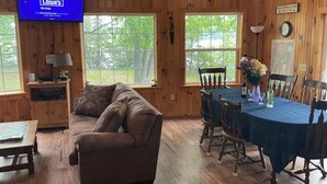 A wooden cabin interior with a couch, dining table, chairs, and a TV displaying Lowe's logo. - BLOW OUT-SALE PRICES!  3 DAY FOLIAGE,Fishing, Dock, Fire Pit, Boat launch & Boat (North Hero)