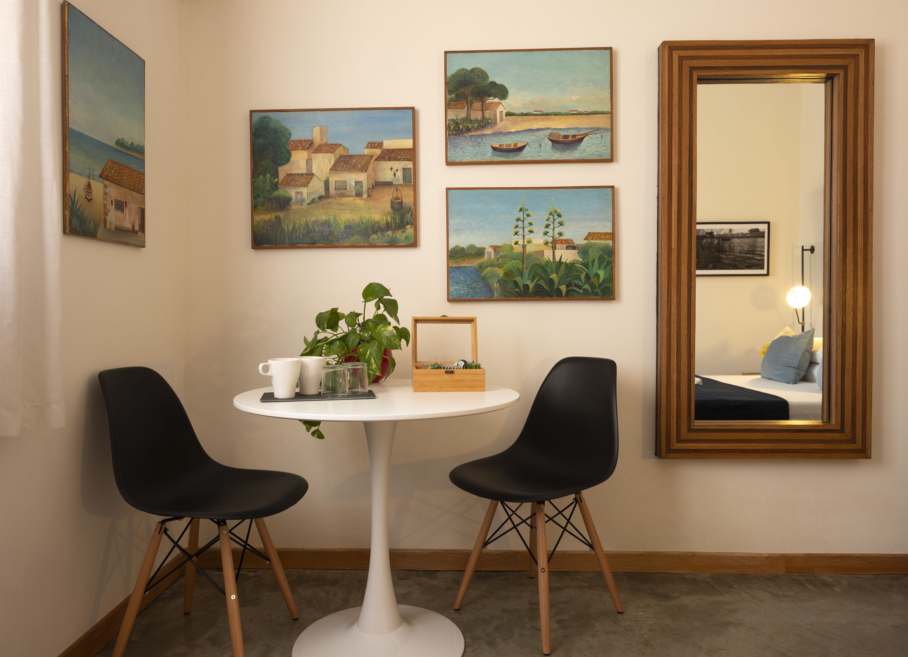 Ein Zimmer mit einem runden weißen Tisch, zwei schwarzen Stühlen, einer Zimmerpflanze und vier Bildern an der Wand.