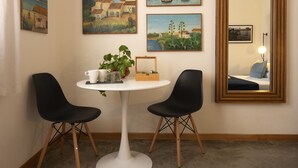 A room with a round white table, two black chairs, a potted plant, and four paintings on the wall. - Stagnone Area Zero (Marsala)