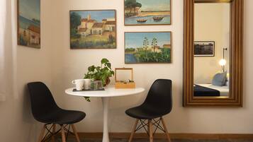 Ein Zimmer mit einem runden weißen Tisch, zwei schwarzen Stühlen, einer Zimmerpflanze und vier Bildern an der Wand.