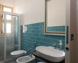 A bathroom with a glass shower enclosure, a toilet, a bidet, and a sink with a mirror above it. - Stagnone Area Zero (Marsala)