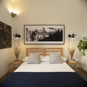 A bedroom with a large bed, two bedside tables, a headboard, a framed picture on the wall, and a potted plant. - Stagnone Area Zero (Marsala)