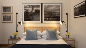 A bedroom with a wooden headboard, two bedside tables with lamps, a bed with white and grey pillows, and three framed black and white photographs on the wall. - Stagnone Area Zero (Marsala)