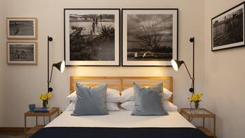 Ein Schlafzimmer mit einem hölzernen Kopfende, zwei Nachttischen mit Lampen, einem Bett mit weißen und grauen Kissen und drei gerahmten Schwarz-Weiß-Fotos an der Wand.