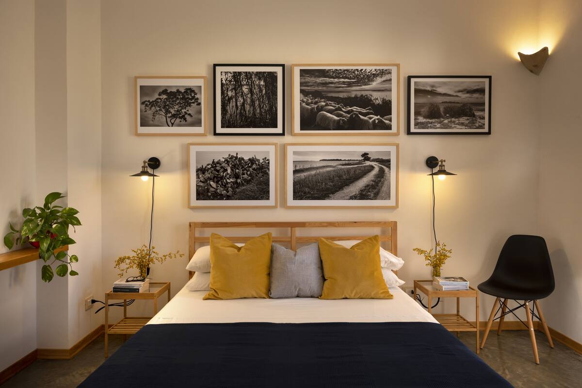 A bedroom with a bed, bedside tables, lamps, a chair, and wall-mounted artwork.