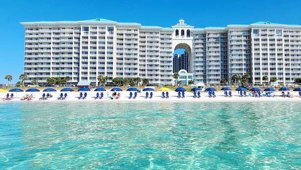 A large hotel with multiple floors, a central archway, and a beach with rows of umbrellas. - BOB AND MARY'S BEACH RETREAT,  FABULOUS GULF VIEWS, GREAT 5  STAR REVIEWS.. (Destin)