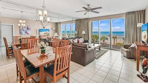 A spacious living area with a balcony overlooking the ocean, a dining area with wooden furniture, and a ceiling fan. - BOB AND MARY'S BEACH RETREAT,  FABULOUS GULF VIEWS, GREAT 5  STAR REVIEWS.. (Destin)