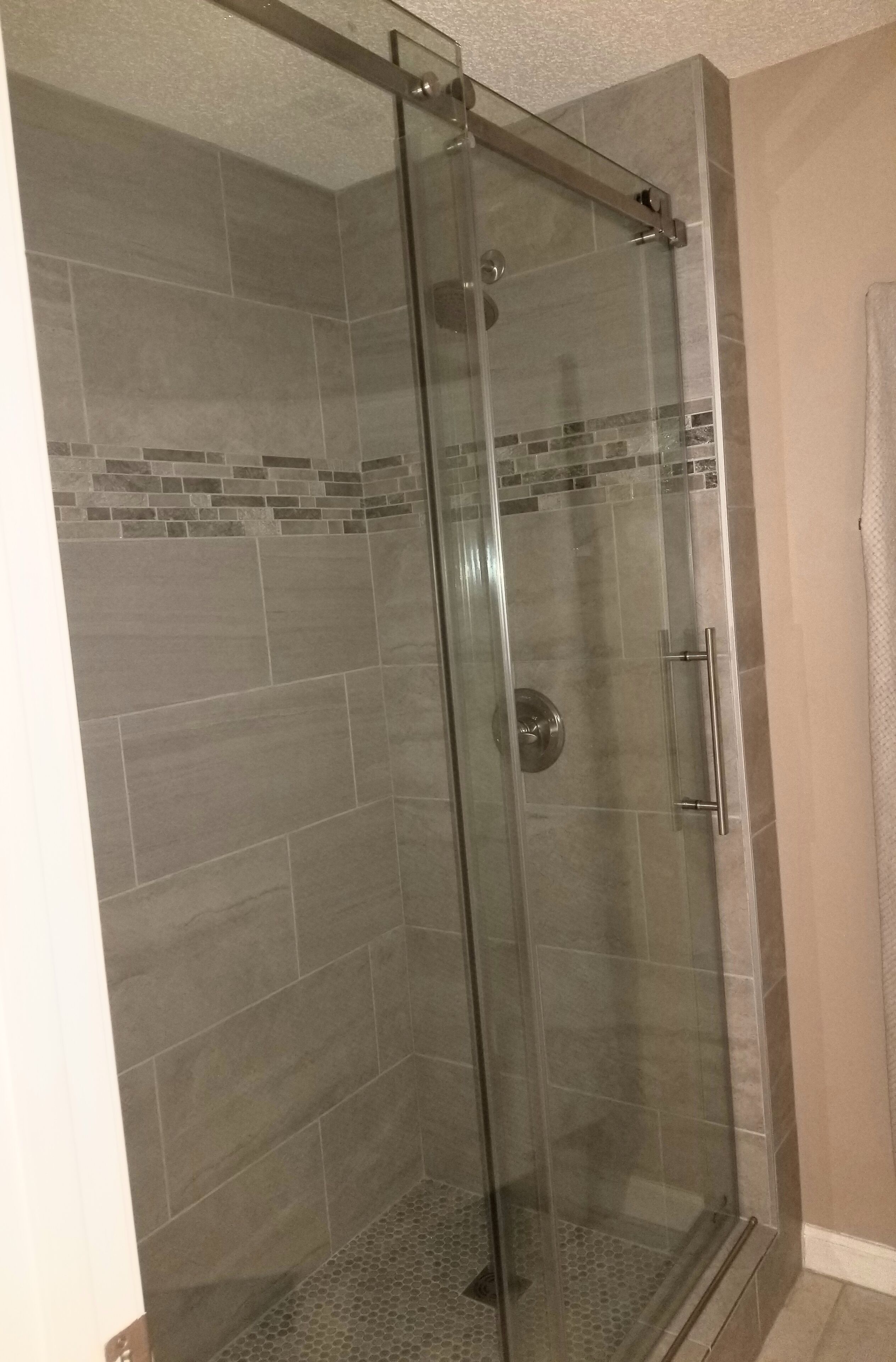 Une douche fermée par des parois de verre, avec un sol carrelé et une poignée en métal.