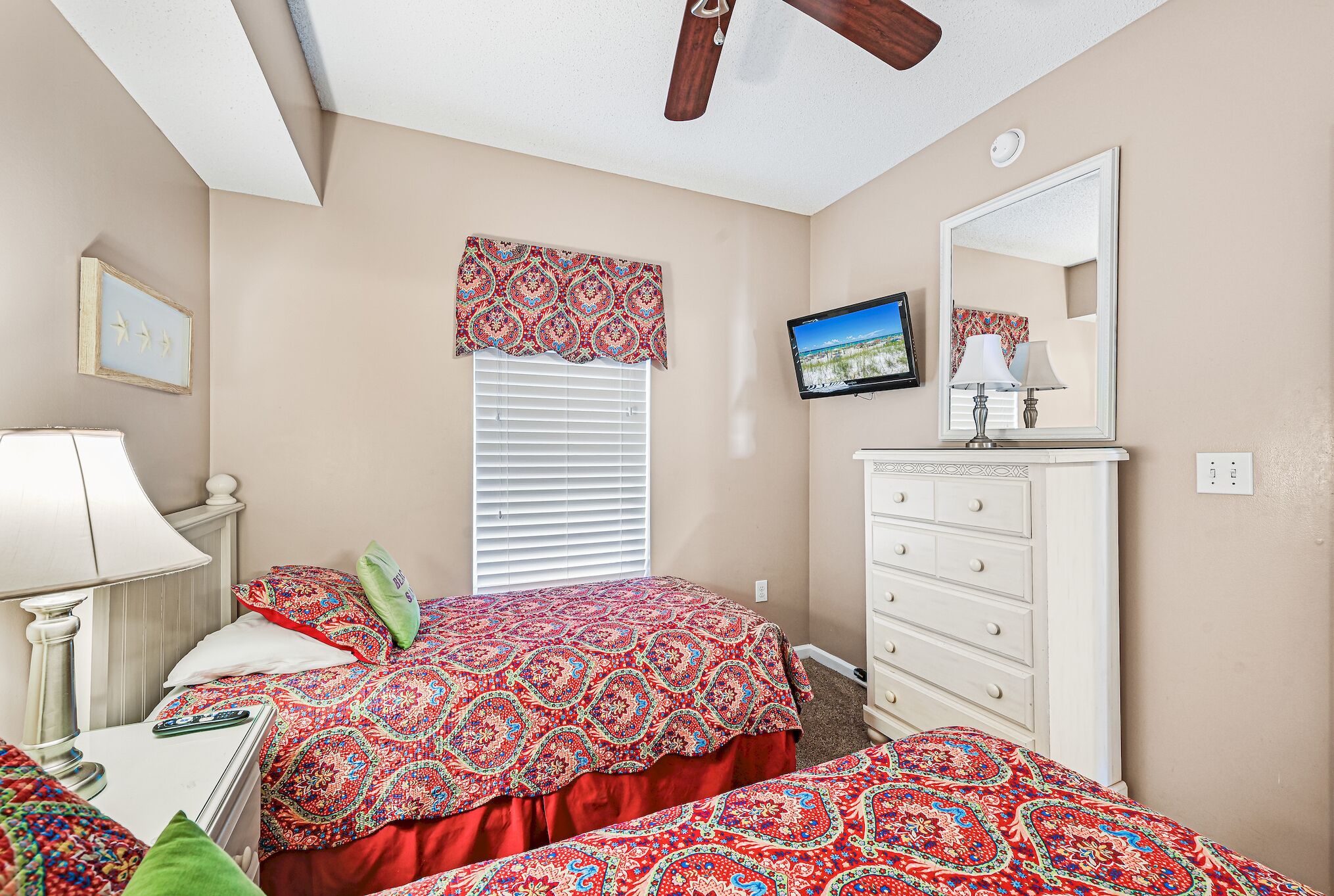 A bedroom with two beds, a dresser, a TV, and a ceiling fan.