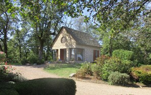 Surrounded by lush greenery, this charming cottage features a stone chimney and a cozy porch area.