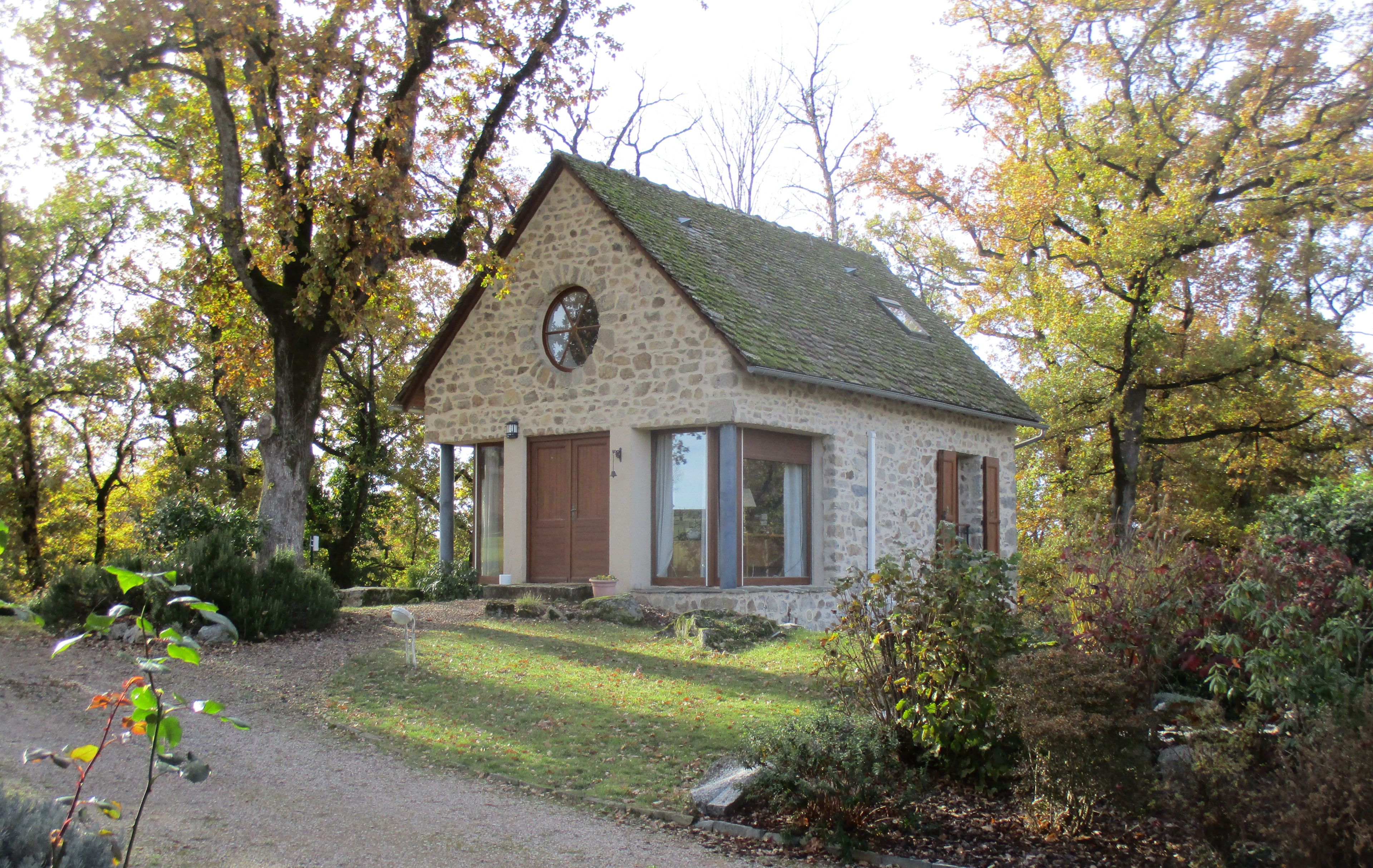 Een stenen huis met een zadeldak, grote ramen en een deur.