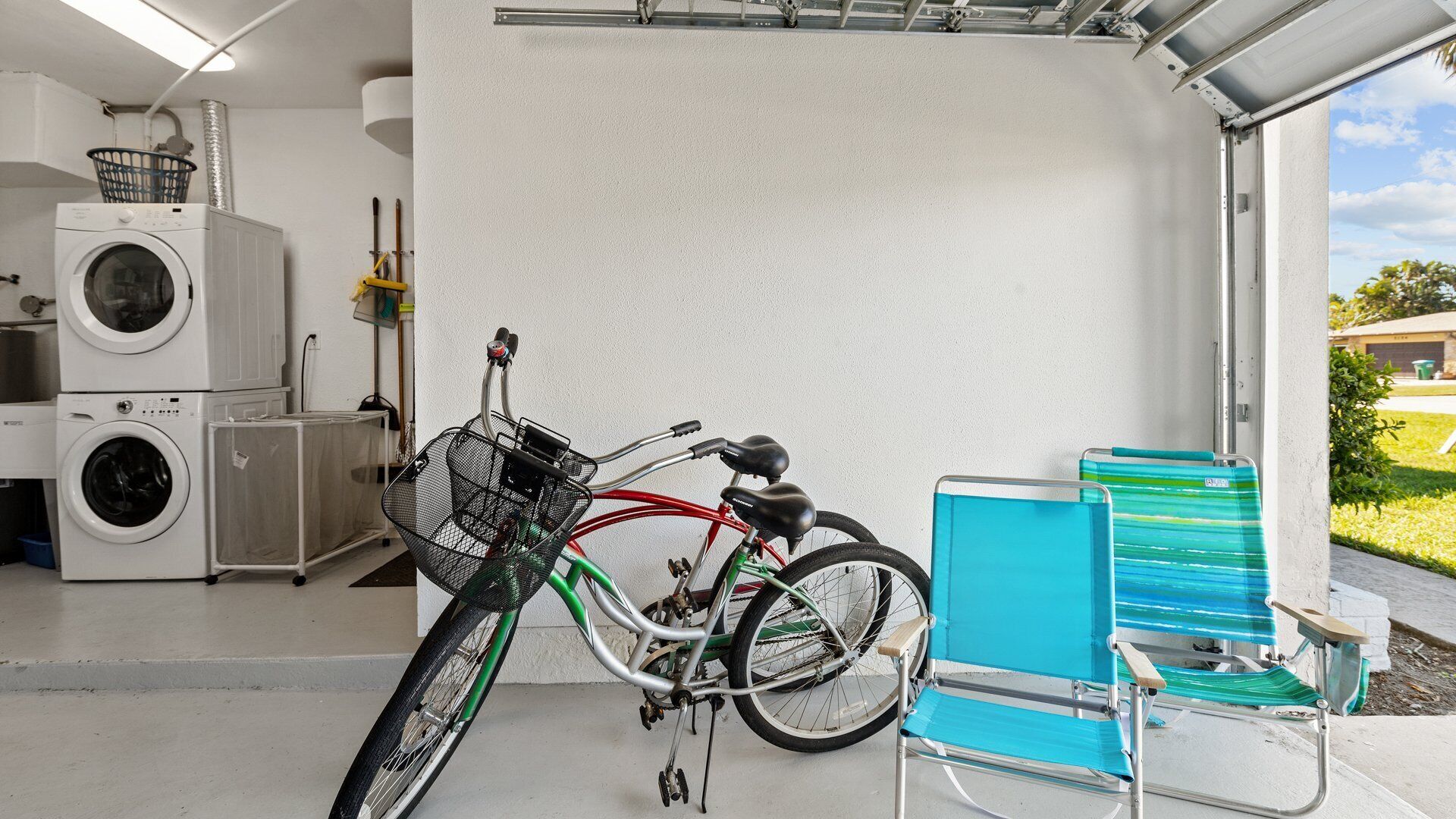 Una sala de bugaderia amb rentadores apilades, una bicicleta amb cistella i una cadira de platja blava.