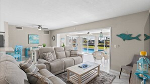 Amplia sala de estar con un juego de sofá color crema, una mesa de centro de madera y vista a una piscina a través de amplios ventanales.