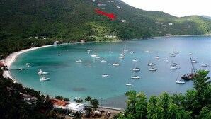 Una zona costera con numerosos barcos anclados en aguas turquesas, rodeada de colinas verdes exuberantes y una playa.