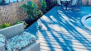 Une terrasse en bois avec un espace salon, entourée d’une végétation tropicale luxuriante et d’une piscine.