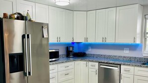 Une cuisine moderne avec des meubles blancs, des appareils en acier inoxydable et un éclairage LED bleu sous les meubles.