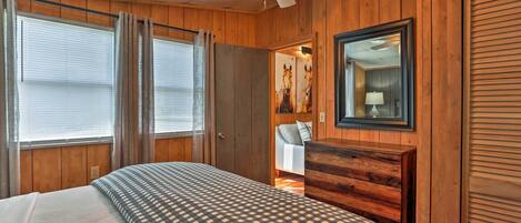 A bedroom with a bed, wooden walls, a ceiling fan, a dresser, and a mirror.